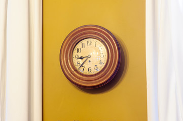 an old vintage clock ticking against an ochre wall with some  white curtains