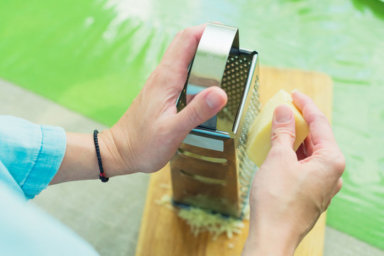 Close-up of a woman's hands rub the parmesan cheese on a metal grater.
