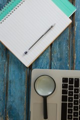 Blank book, pen, magnifying glass and laptop on wooden plank