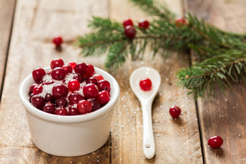 A small bowl of cranberries with sugar on a wooden table with scattered berries and a white spoon © ozhukovaphoto