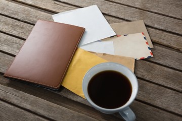 Coffee with various envelopes and diary on wooden plank