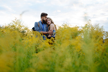 Naklejka na ściany i meble Young couple in love dressed in country style standing on field of flowers