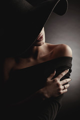 Dark studio portrait of elegant woman in black wide hat and black dress. Hidden half face. - 183926586
