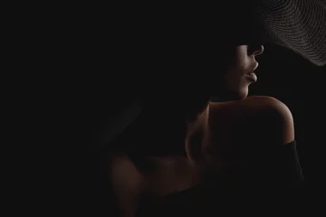 Selbstklebende Fototapete Frauen Dramatisches dunkles Studioporträt einer eleganten und sexy Frau in schwarzem, breitem Hut und schwarzem Kleid. Verstecktes halbes Gesicht.