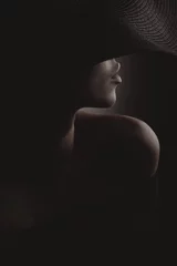Dramatisches dunkles Studioporträt einer sexy Frau mit schwarzem breitem Hut und schwarzem Kleid. Verstecktes halbes Gesicht. © monchak