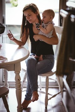 Mother Using Mobile Phone While Holding Her Baby