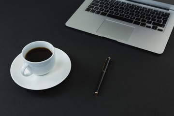 Black coffee, pen and laptop on black background
