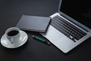 Pen, organizer, black coffee and laptop on black background