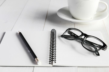Business accessories on white wooden table : notebook,pencil, glasses,cup.