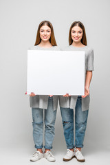 beautiful smiling twins holding blank banner in hands isolated on grey
