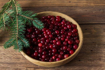 Red berries in a wooden plate on a wooden background with spruce branches. Cranberry.