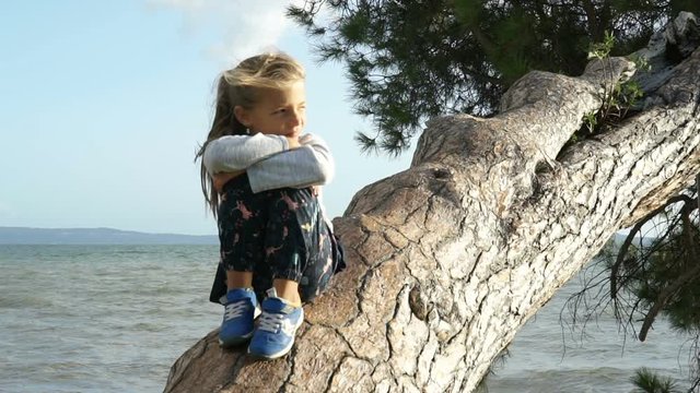 September 2017 -Bolsena, Italy - Little girl sitting on the bended tree over the lake, slowmo