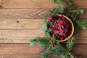 Red berries in a wooden plate on a wooden background with spruce branches. Cranberry. - 183929529