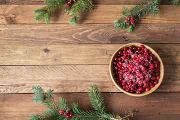 Red berries in a wooden plate on a wooden background with spruce branches. Cranberry. - 183929587