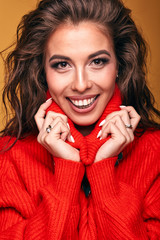 Bright portrait of attractive and smiling brunette woman wearing orange red sweater and turquoise skirt in studio with orange background