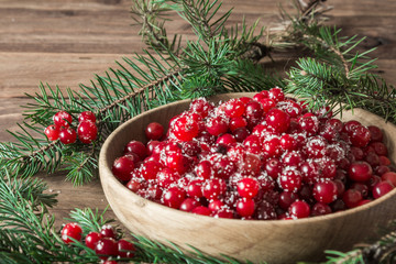 Red berries in a wooden plate on a wooden background with spruce branches. Cranberry. - 183929794