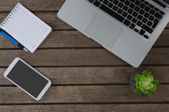 Laptop, pot plant, notepad, pen and mobile phone on wooden plank