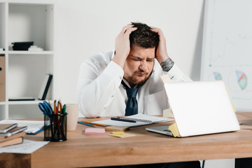 overweight businessman with headache using laptop in office
