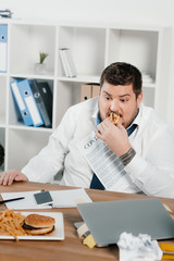 fat businessman eating hamburgers and french fries in office