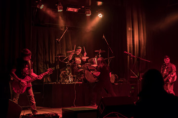 Drummer and three guitarists at a concert with red lights, in the smoke
