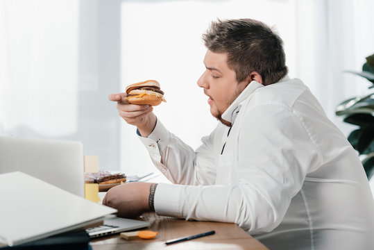 overweight businessman eating hamburger while working in office