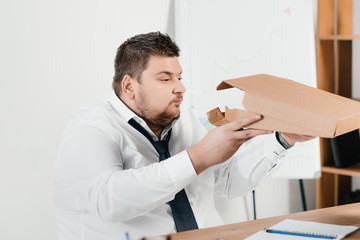 overweight businessman eating pizza at workplace