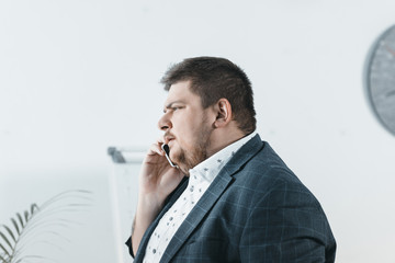 overweight businessman talking on smartphone in office