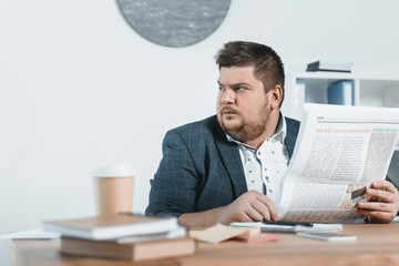 overweight businessman in suit reading newspaper at workplace