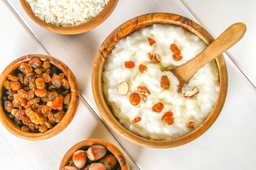 Rice milk porridge with nuts and raisins in wooden bowls on a white wooden table.