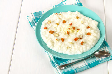 Rice milk porridge with nuts and raisins in a blue dish on a white wooden table.