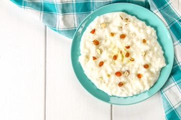 Rice milk porridge with nuts and raisins in a blue dish on a white wooden table.