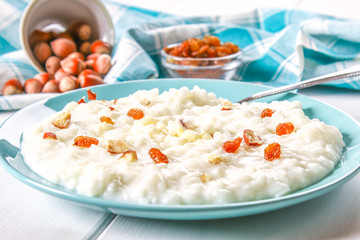 Rice milk porridge with nuts and raisins in a blue dish on a white wooden table.