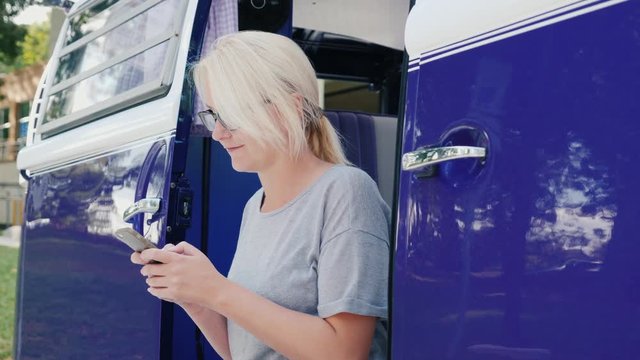A woman is using a smartphone. Sits on the step of the violet retro van