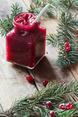 Cranberry jam in a jar on a wooden background with spruce branches. - 183933523