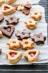 Different shapes of festive cookies with jam on a baking paper.
