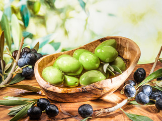 Whole table olives in the wooden bowl on the table.