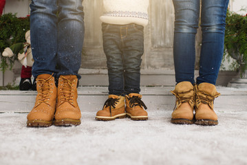 Legs of parents with little son. Child boy in sweater staying near porch snow steps at light house with decorated in red green New Year home. Christmas good mood. Family on holiday 2018. Bottom view