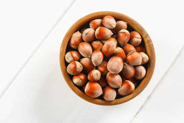 Hazelnut nuts in a wooden bowl on a white wooden table. Superfood.