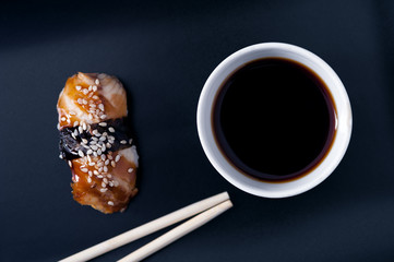 Eel sashimi roll, soy sauce and chopsticks on dark background, top view