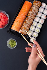 Popular Japanese food - Sushi rolls set with wasabi, ginger and chopsticks, top view. Female hands holding chopsticks.