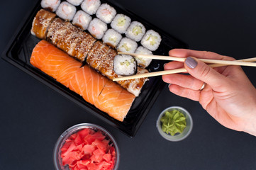 Popular Japanese food - Sushi rolls set with wasabi, ginger and chopsticks, top view. Female hands holding chopsticks with roll.