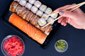 Popular Japanese food - Sushi rolls set with wasabi, ginger and chopsticks, top view. Female hands holding chopsticks with roll.