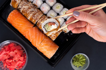Popular Japanese food - Sushi rolls set with wasabi, ginger and chopsticks, top view. Female hands holding chopsticks with roll.