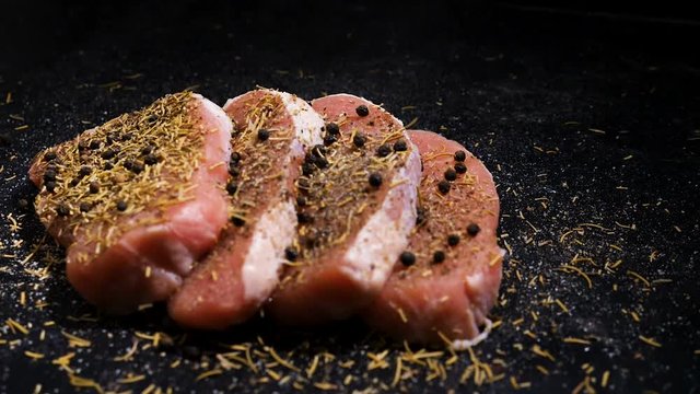 Slow motion cran shot of four juicy and delicious four seasoned pork steaks on black wooden board