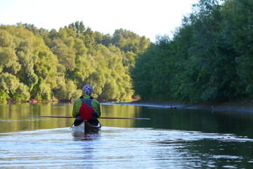 Fototapeta na wymiar Man in brown wooden handmade kayak paddling at river on biosphere reserve in spring. Kayaking in Danube river