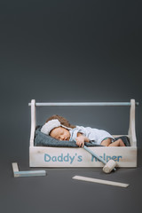 adorable baby with hammer in hand sleeping in wooden toolbox with daddys helper lettering