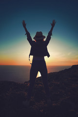 Fototapeta na wymiar Carefree womans silhouette hands up in sunset on cliff