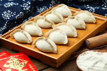 Fototapeta na wymiar raw dumplings on wooden plate with flour and rolling pin and red packet,Chinese word translation:happiness