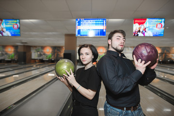 A young man and a girl posing on a camera with balls for bowling in the hands of the background of...