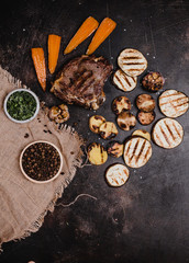 top view of delicious grilled steak and sliced vegetables on black concrete surface